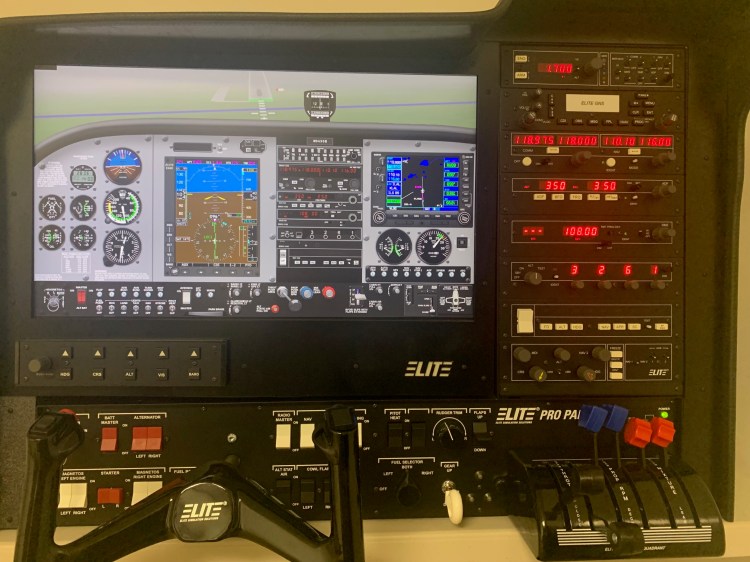 Flight simulator cockpit panel with digital displays, navigation instruments, throttle controls, and avionics stack used for pilot training.